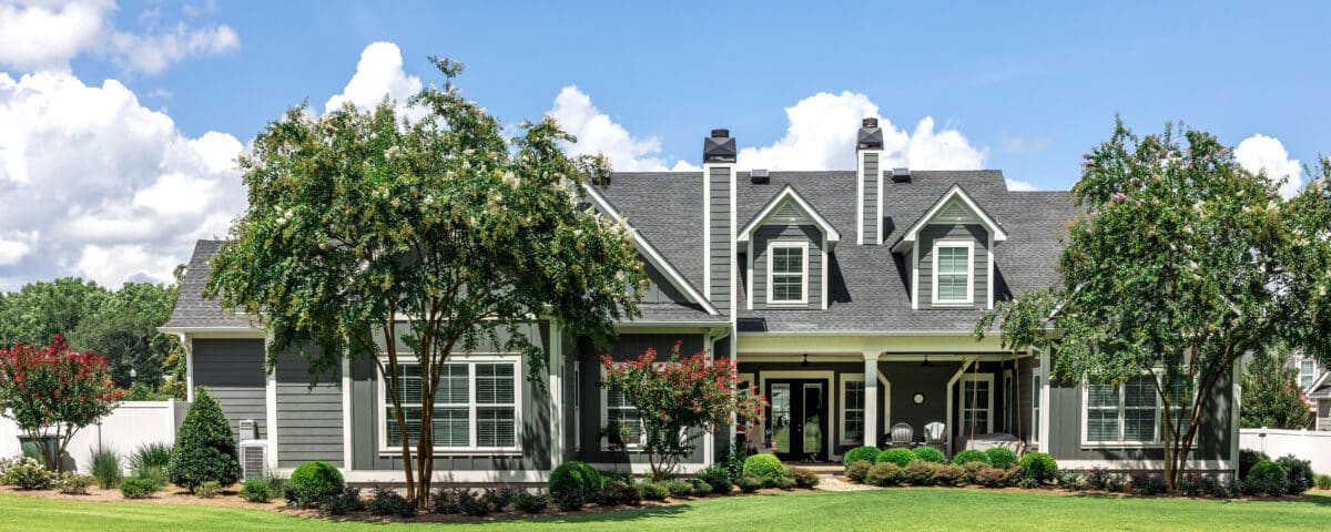 The rear view of a large gray craftsman new construction house with a landscaped yard and a garage and driveway